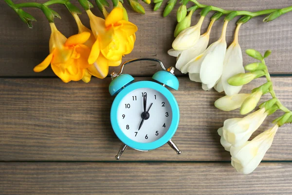 Wecker und schöne Blumen auf blauem Holzgrund — Stockfoto