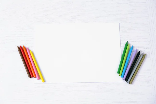 Kleurpotloden en blanco papier blad op houten tafel — Stockfoto