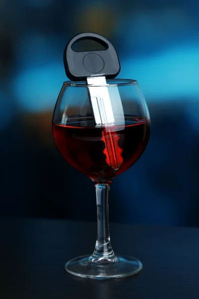 Композиция с ключом от машины и бокалом красного вина, на деревянном столе, на ярком фоне — стоковое фото
