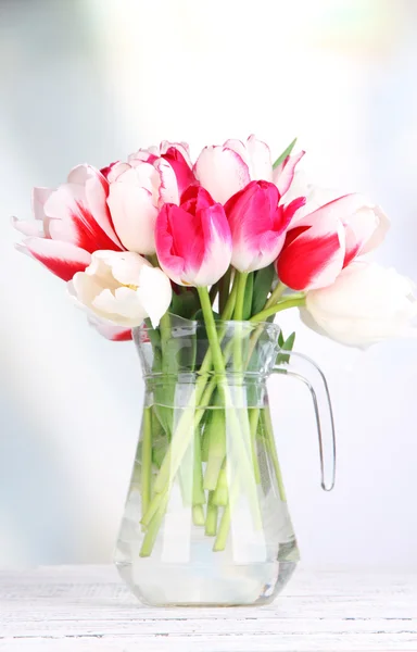 Beautiful tulips in glass jug on light background — Stock Photo, Image