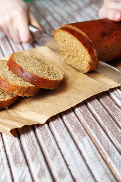 Mani femminili taglio del pane su tavola di legno, primo piano — Foto Stock