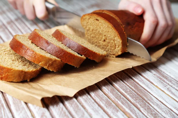 Mani femminili taglio del pane su tavola di legno, primo piano — Foto Stock