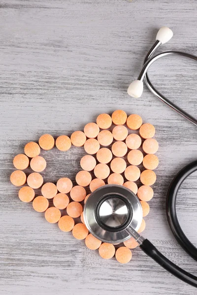 Heart of pills and stethoscope on wooden background — Stock Photo, Image