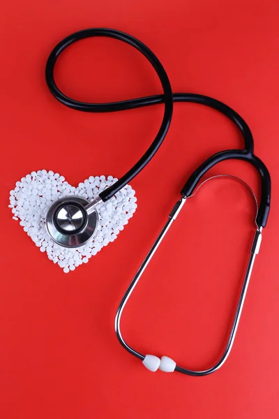 Coeur de pilules et stéthoscope sur fond rouge — Photo