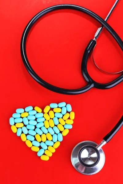 Srdce pilulek a stetoskop na červeném pozadí — Stock fotografie