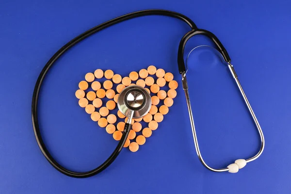 Coeur de pilules et stéthoscope sur fond bleu — Photo