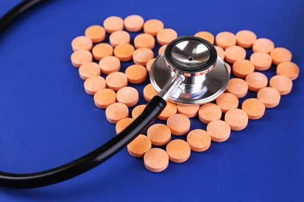 Hart van pillen en stethoscoop op blauwe achtergrond — Stockfoto