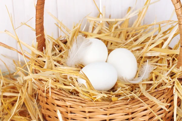 White eggs in a wicker bascet on straw on white wooden background close-up — Stock Photo, Image