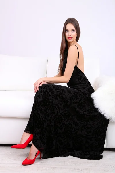 Schöne junge Frau in schwarzem Kleid auf Sofa auf weißem Hintergrund — Stockfoto