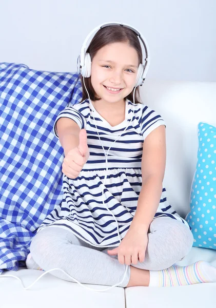 Mooi meisje, zittend op een bank en luisteren naar muziek, op huis interieur achtergrond — Stockfoto