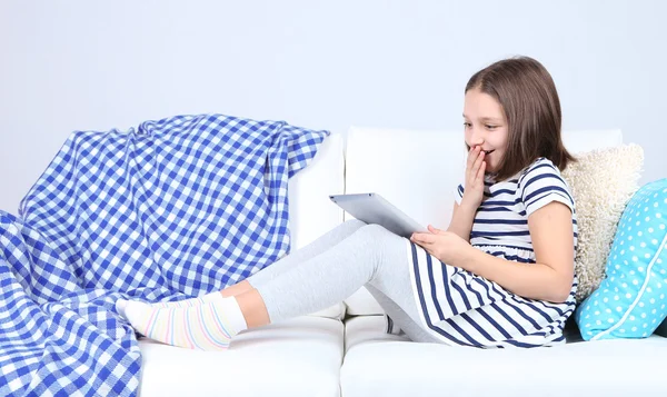 Menina bonita sentada no sofá com tablet, em casa fundo interior — Fotografia de Stock