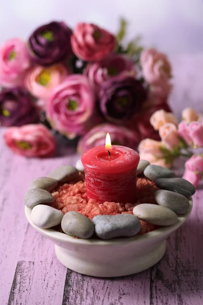 Композиция со спа-камнями, свечами и цветами на цветном деревянном столе, на светлом фоне — стоковое фото