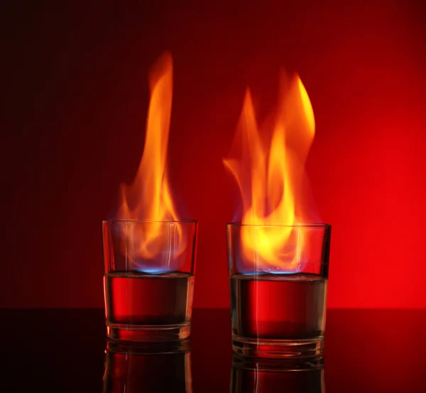 Glasses with burning alcohol on red background — Stock Photo, Image