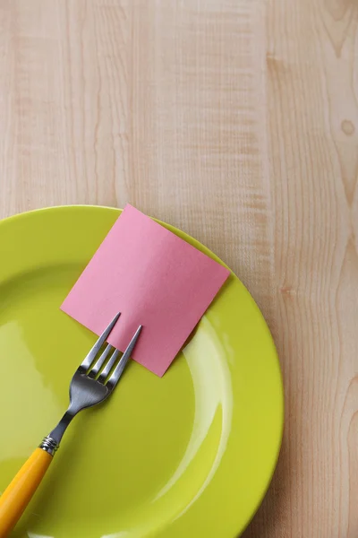 Empty note paper attached to fork, on plate, on color wooden background — Stock Photo, Image