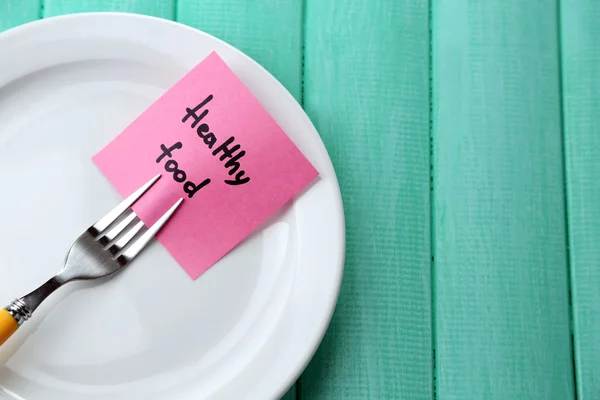 Note paper with message  attached to fork, on plate, on wooden background — Stock Photo, Image