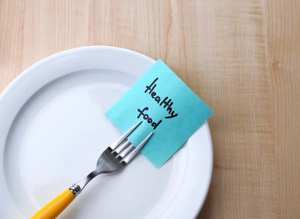 Note paper with message  attached to fork, on plate, on color wooden background — Stock Photo, Image