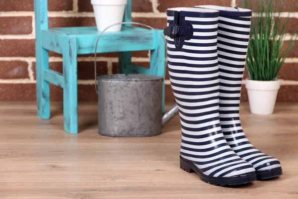 Paar van kleurrijke gumboots, plant in pot, stoel en gieter op kleur muur achtergrond — Stockfoto