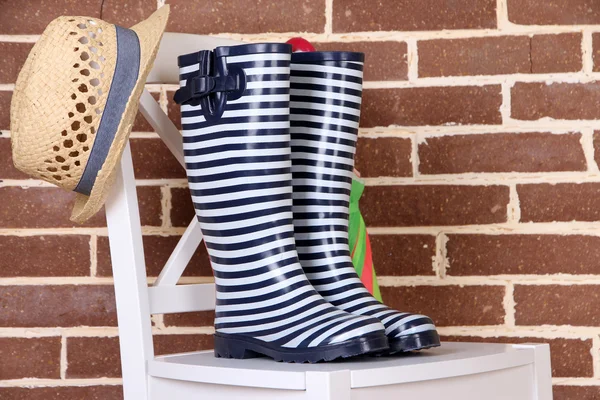 Par de botas de goma de colores en la silla sobre fondo de pared de color —  Fotos de Stock