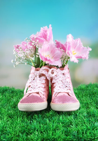 Schöne Gummischuhe mit Blumen drinnen auf grünem Gras, auf hellem Hintergrund — Stockfoto