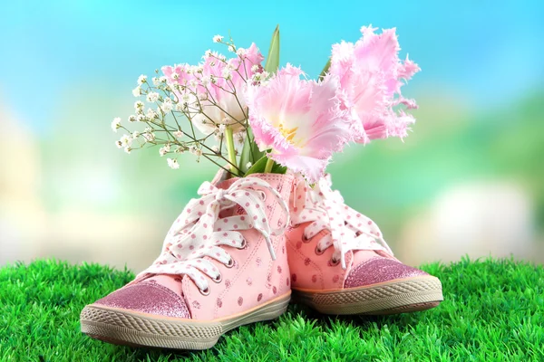 Schöne Gummischuhe mit Blumen drinnen auf grünem Gras, auf hellem Hintergrund — Stockfoto