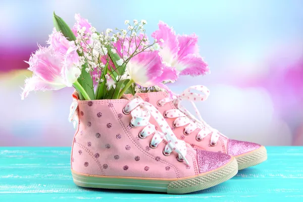 Hermosos zapatos de goma con flores en el interior en la mesa de madera, sobre fondo brillante —  Fotos de Stock