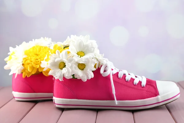 Bellissime scarpe da ginnastica con fiori all'interno su tavolo in legno, su sfondo chiaro — Foto Stock