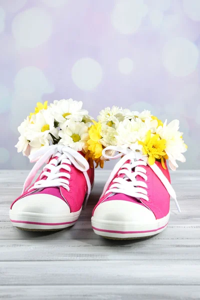 Schöne Gummischuhe mit Blumen drinnen auf Holztisch, auf hellem Hintergrund — Stockfoto