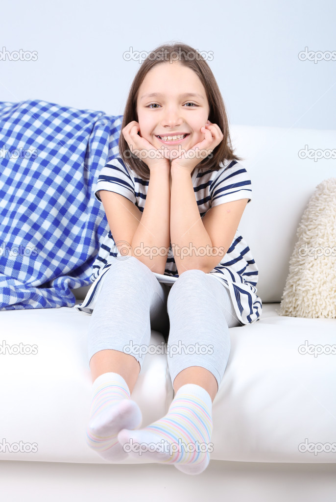 Beautiful little girl sitting on sofa, on home interior background