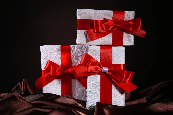 Schöne Geschenke mit roten Bändern auf Seide, auf dunklem Hintergrund — Stockfoto