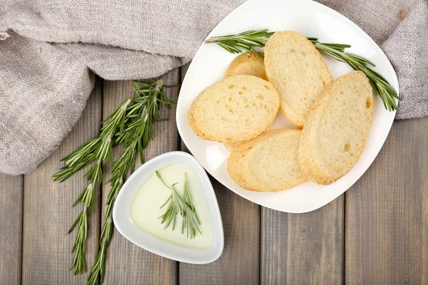 Fresh bread with olive oil and rosemary on wooden table — Stock Photo, Image