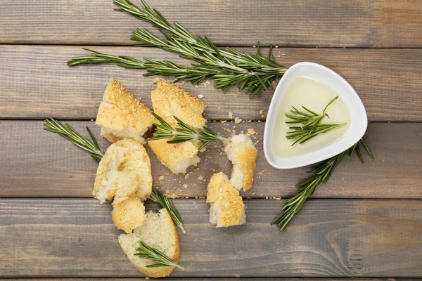 Fresh bread with olive oil and rosemary on wooden table — Stock Photo, Image