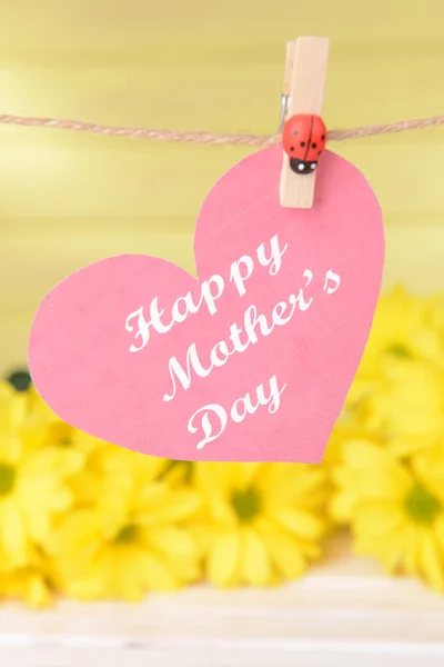 Feliz Día de las Madres mensaje escrito en papel corazón con flores sobre fondo amarillo —  Fotos de Stock
