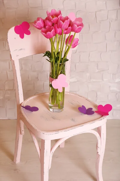 Sammansättning med bukett tulpaner i vas, på stol, på vägg bakgrund — Stockfoto