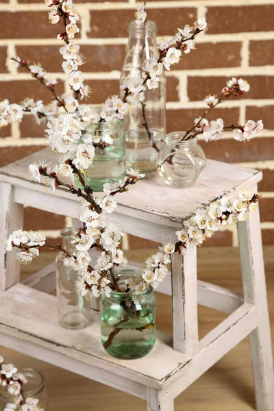 Beautiful apricot blossom in transparent jars on brick wall background — Stock Photo, Image