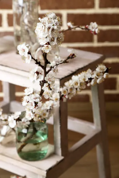 Beautiful apricot blossom in transparent jars on brick wall background — Stock Photo, Image