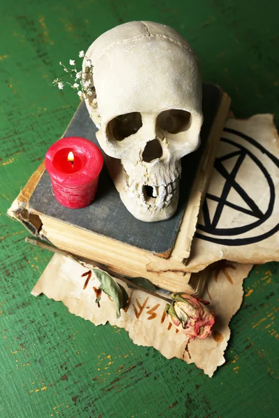 Skull on old book, candle and dry rose  on color wooden background — Stock Photo, Image