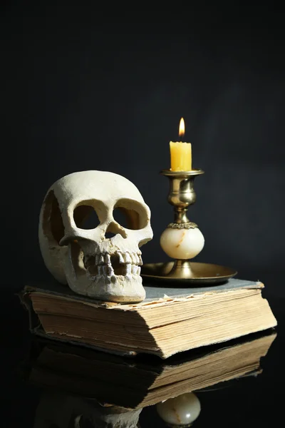 Teschio e candela su vecchio libro su sfondo di colore scuro — Foto Stock