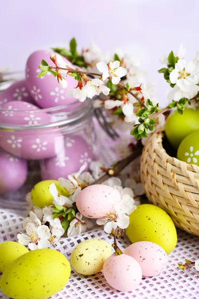 Composizione con uova di Pasqua in vaso di vetro e cesto di vimini, e rami fioriti su fondo chiaro — Foto Stock