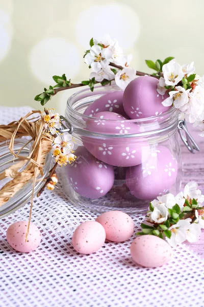 Composition with Easter eggs in glass jar and blooming branches on light background — Stock Photo, Image