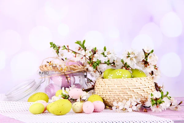 Composición con huevos de Pascua en tarro de vidrio y canasta de mimbre, y ramas florecientes sobre fondo claro — Foto de Stock