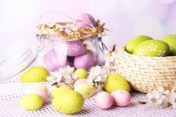 Samenstelling met Pasen eieren in glazen pot en rieten mand en bloeiende takken op lichte achtergrond — Stockfoto