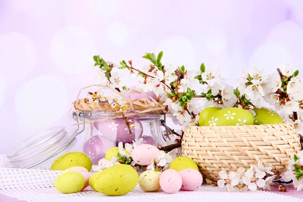 Состав с пасхальными яйцами в стеклянной банке и плетеной корзине, и цветущие ветви на светлом фоне — стоковое фото