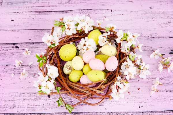 Composition with Easter eggs and blooming branches in nest, on wooden background — Stock Photo, Image