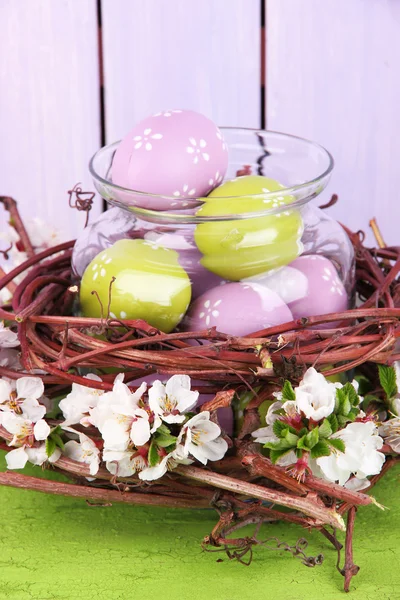 Composition avec oeufs de Pâques et branches en fleurs dans un bocal en verre et un nid décoratif, sur fond de bois de couleur — Photo