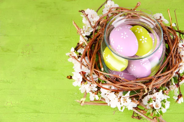 Composición con huevos de Pascua y ramas florecientes en tarro de vidrio y nido decorativo, sobre fondo de madera de color —  Fotos de Stock