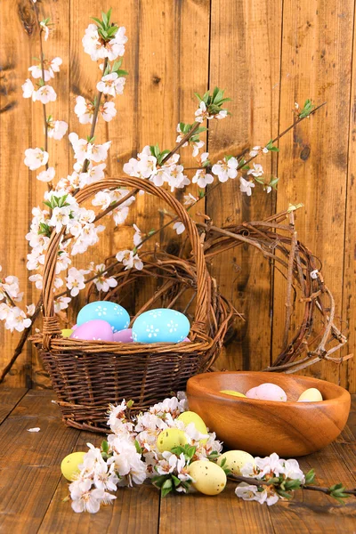 Composition with blooming branches and Easter eggs in wooden bowl, wicker basket on wooden background — Stock Photo, Image