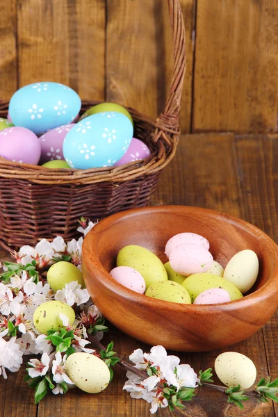 Composizione con rami fioriti e uova di Pasqua in ciotola di legno, cestino di vimini su fondo di legno — Foto Stock