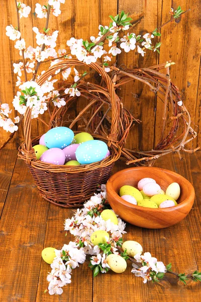 Composizione con rami fioriti e uova di Pasqua in ciotola di legno, cestino di vimini su fondo di legno — Foto Stock