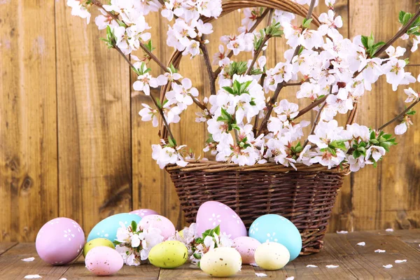 Состав с цветущими ветвями и пасхальными яйцами в плетеной корзине на деревянном фоне — стоковое фото