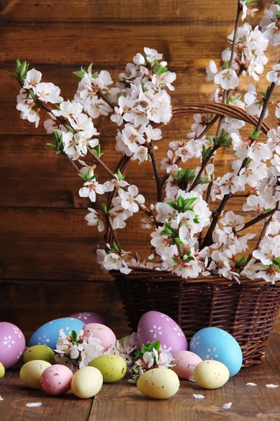 Composición con ramas florecientes y huevos de Pascua en canasta de mimbre sobre fondo de madera —  Fotos de Stock